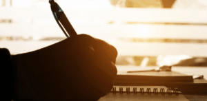 Silhouette of hand writing in notebook with soft sunlight through window in background