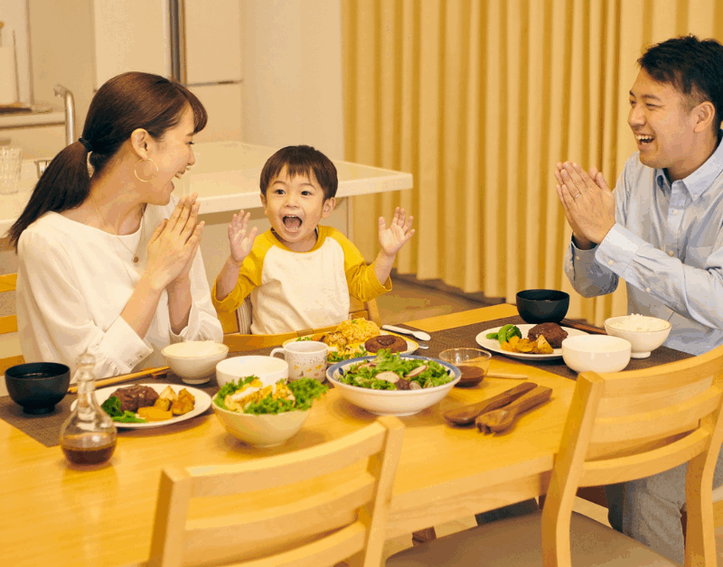Happy family claps and smiles around a dinner table, enjoying a healthy homemade meal together in a warm kitchen