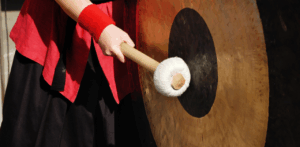 Person striking a large gong with a padded mallet during a cultural event