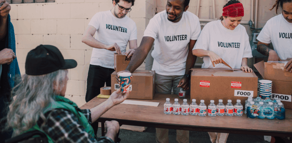 Volunteers distribute food and water to a seated elderly person at a donation event, promoting community outreach