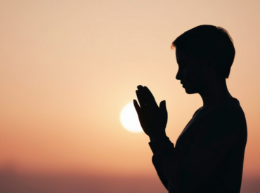 Silhouette of woman praying at sunset with hands together