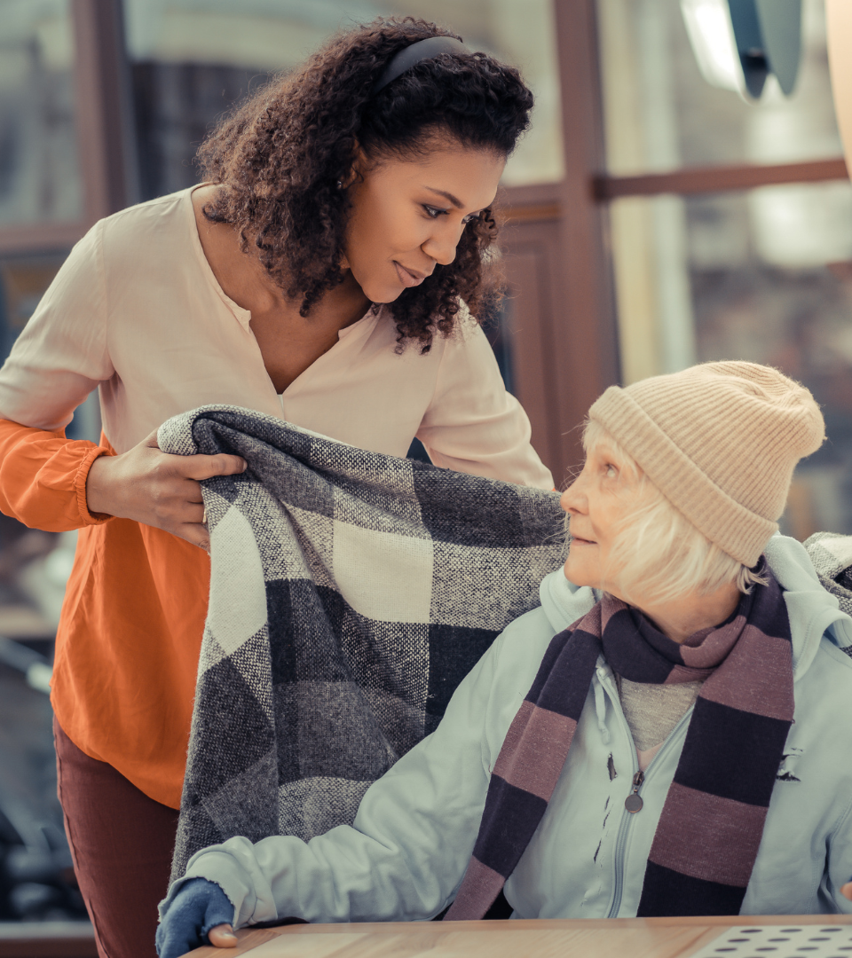 Caregiver gently placing a blanket over an elderly woman, showing compassion, support, and senior care assistance