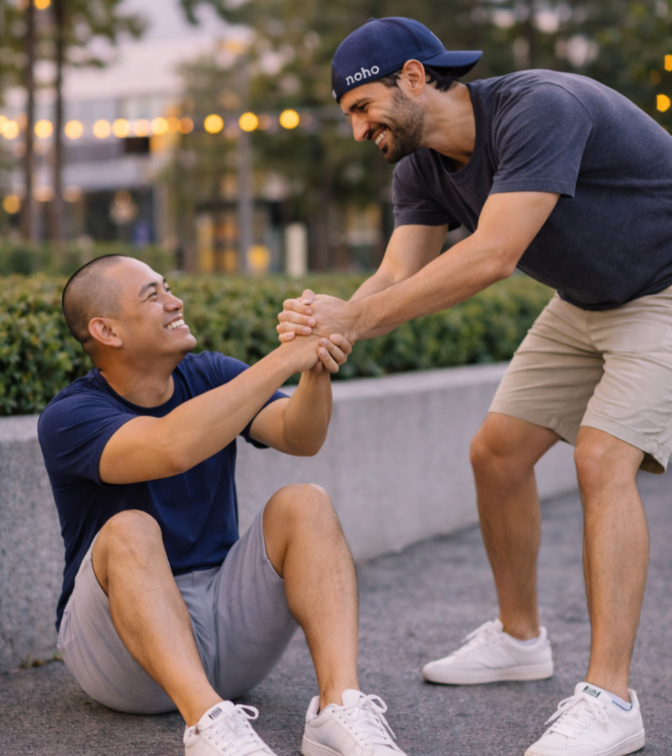 Two men smiling as one helps the other up from the ground outdoors, showing friendship, support, and teamwork